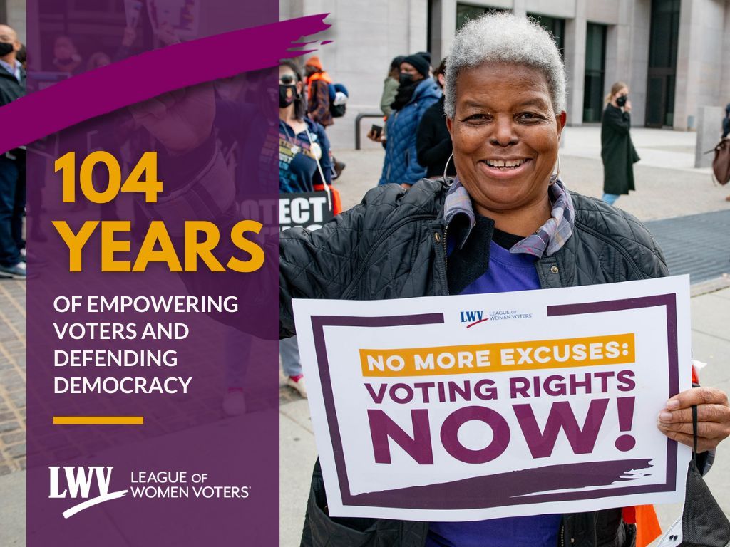 A photo of LWVUS 20th president Dr. Deborah Turner holding a rally sign. The rally signs says 'NO MORE EXCUSES VOTING RIGHTS NOW!' To the left of Dr. Turner is a purple stripe with a magenta LWV swoosh at the top. Below the swoosh is yellow text that says '104 years' then white text underneath that says 'of empowering voters and defending democracy.'